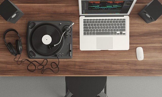 Mesa com laptop, alto falante, toca disco e fone. Boas ferramentas para reproduzir a playlist do seu open house.