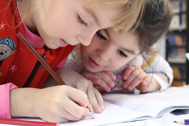 Duas crianças desenhando em uma folha de papel com lápis coloridos.