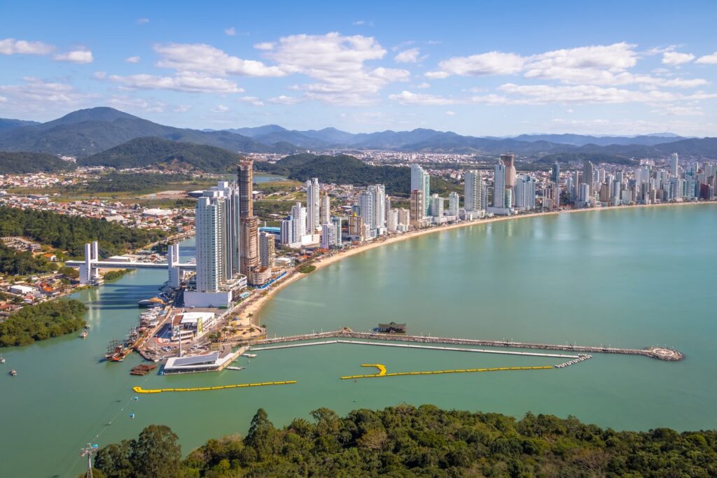 Na orla das praias de Balneário Camboriú, estão localizados muitos edifícios altos, dentre a paisagem montanhosa.