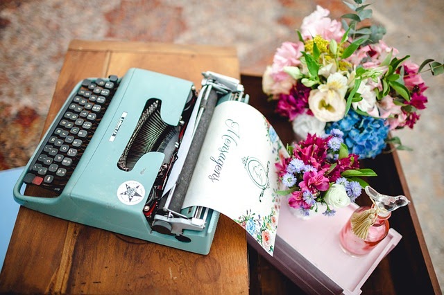 Máquina de escrever vintage e belas flores sobre uma móvel de madeira escura.