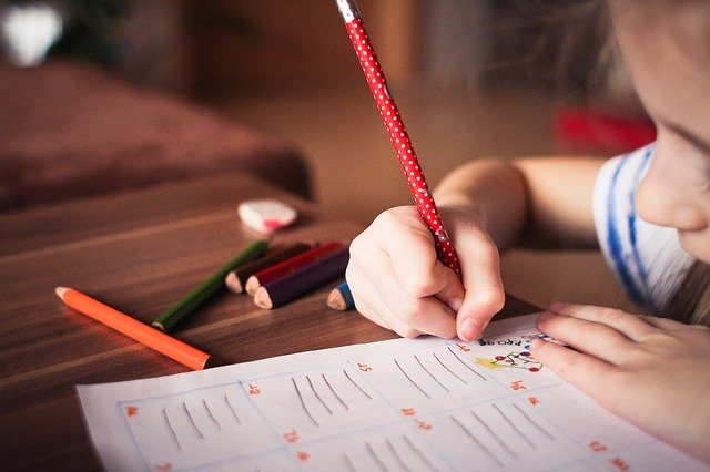 Criança está desenhando sobre uma folha utilizando um lápis de cor.