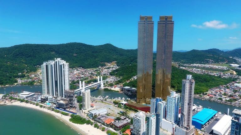Imagem de edifícios em Balneário Camboriú, envoltos por uma bela paisagem com montanhas e praia.