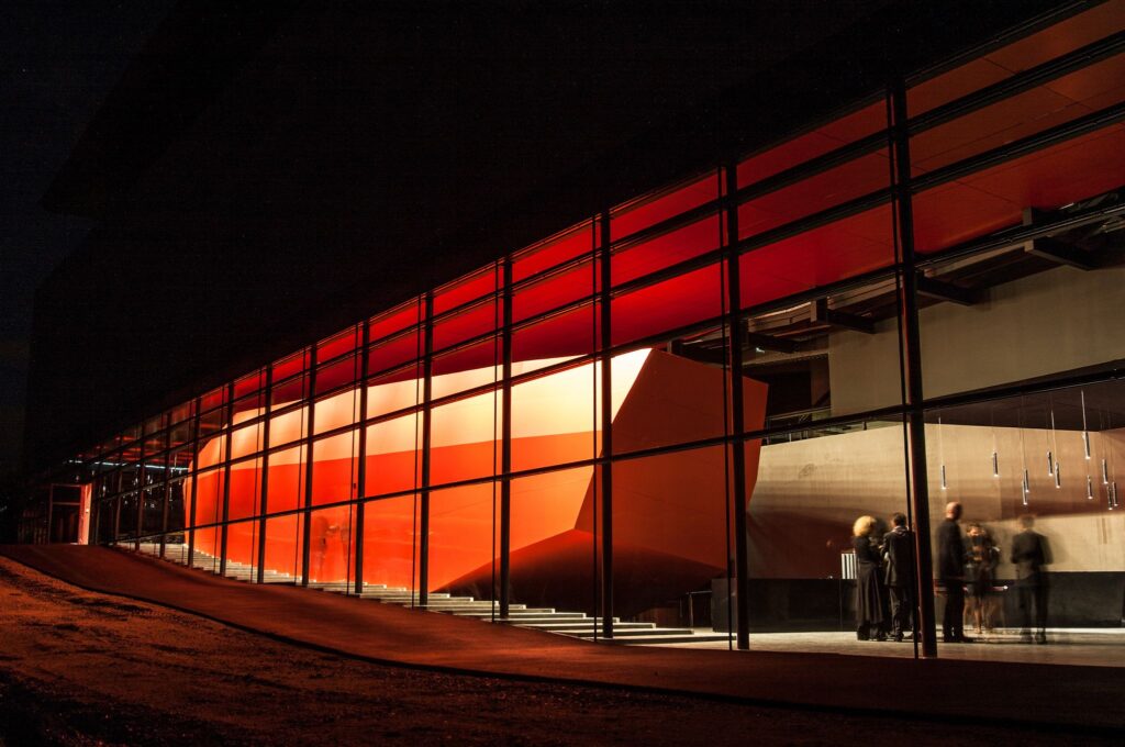 Vista externa do Museu FRAC, com luz interna que permite a visão do grande bloco vermelho.