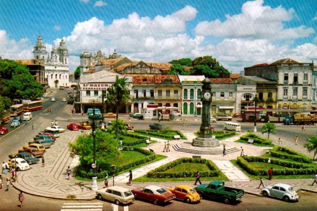 Fotografia antiga da Praça do Relógio, contornada por paisagismo.