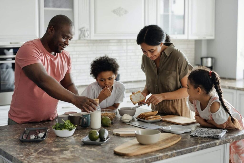 Família com dois adultos e duas crianças se divertindo na cozinha.