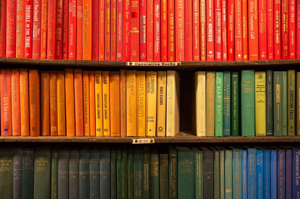 Por cores: como organizar estante de livros pela setorização por cores. Estante com livros de diferentes cores como azul, verde, amarelo, laranja e vermelho.
