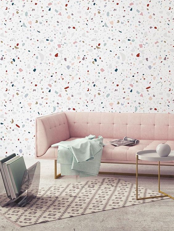 Papel de parede com granilite com fundo branco e pedras coloridas que combinam com o sofá rosa que está na sala.