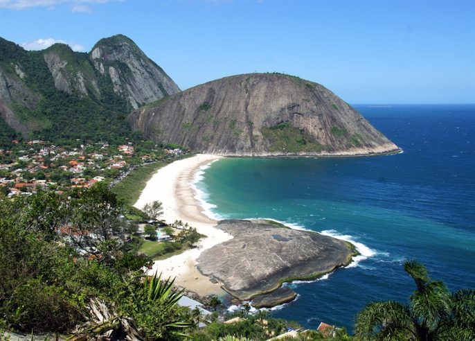 Praia de Itacoatiara com mar azul, montanhas e muita vegetação.