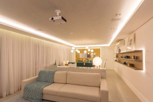Fita de LED posicionada sobre a sanca de gesso, assim a iluminação da sala de estar que foi feita com cores branco e cru, é feita indiretamente.