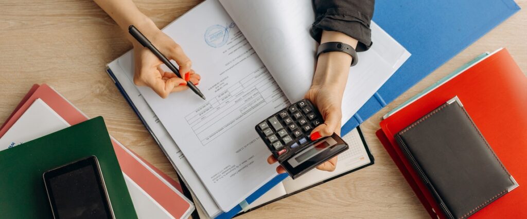 Pessoa com uma calculadora em uma mão e fazendo anotações com a outra, verificando as opções de financiamento.