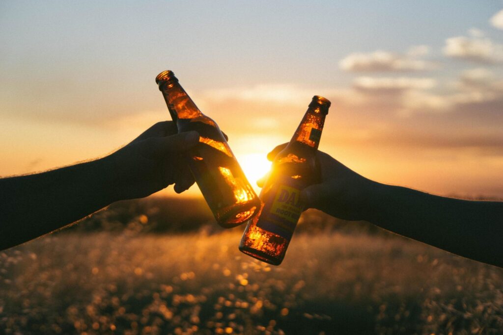 Brinde com garrafas de cerveja e ao fundo paisagem com pôr do sol.
