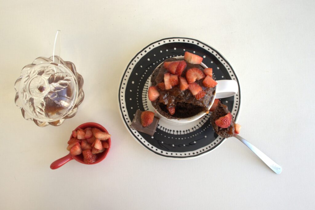 Imagem do bolo de caneca finalizado, coberto por geleia de morango e morangos picados.