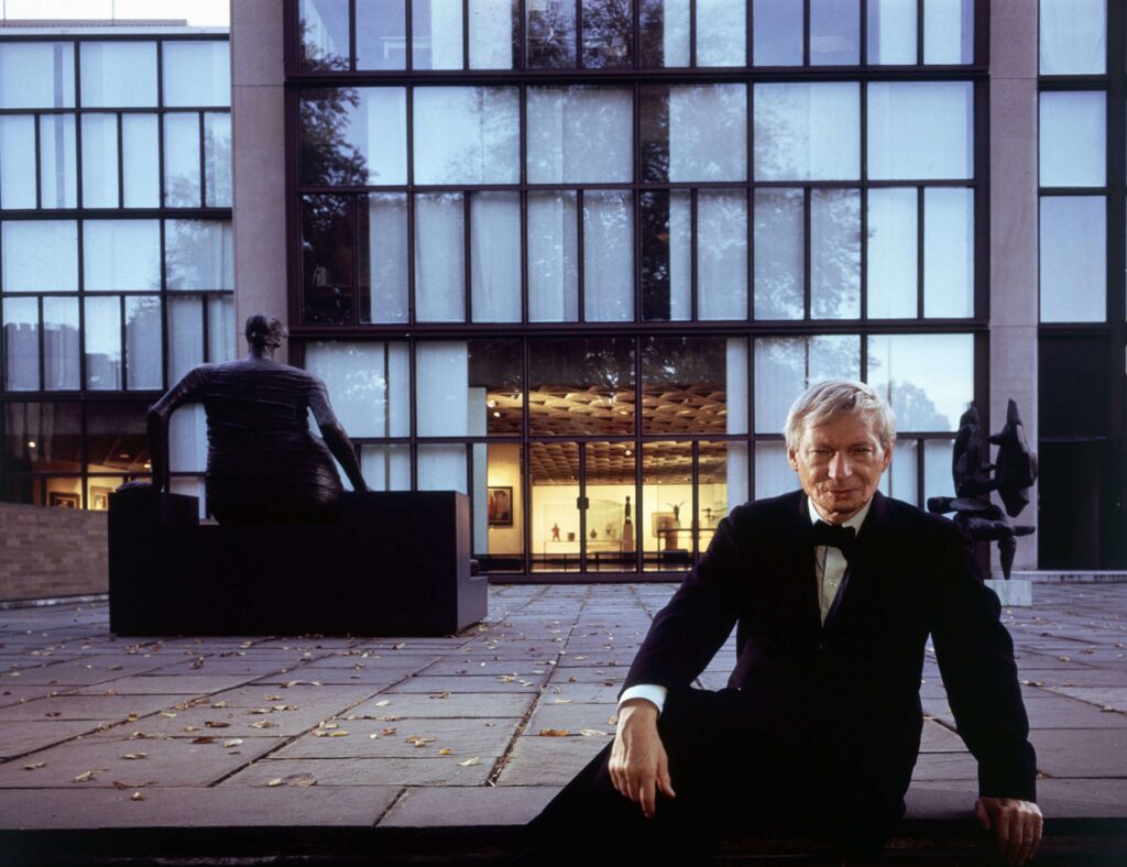 Louis Kahn posando para foto em frente a uma fachada envidraçada do museu.