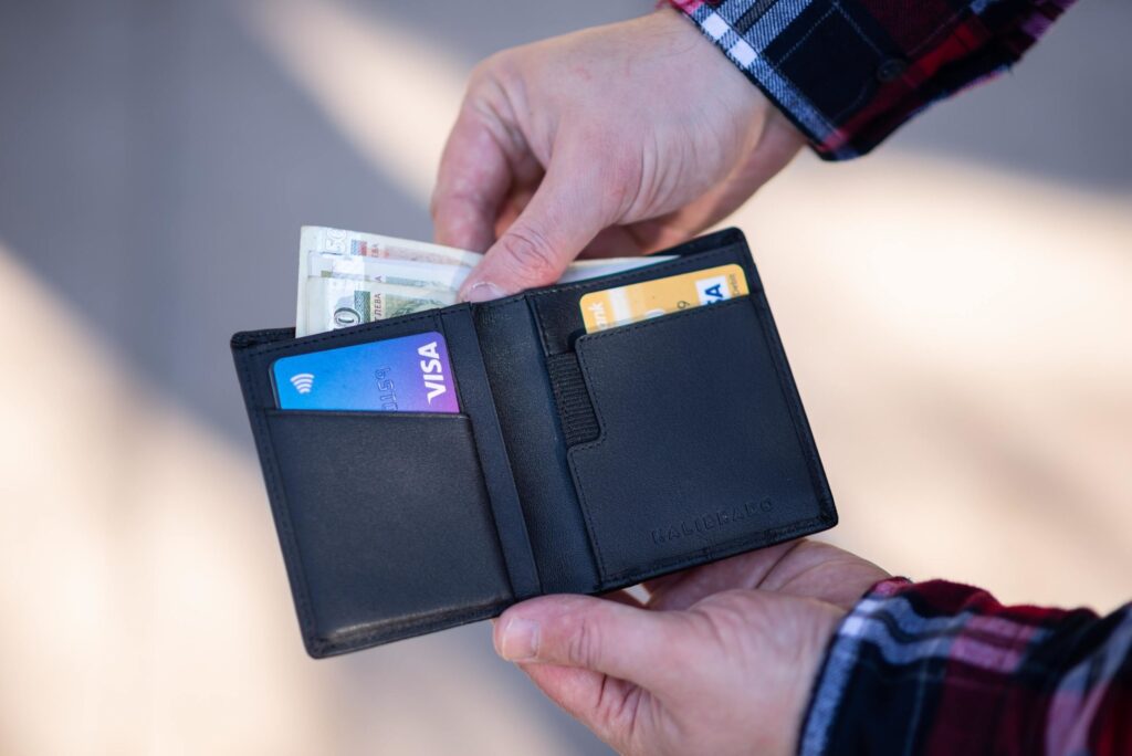 Homem segurando com as mãos uma carteira preta com dinheiro e cartões.