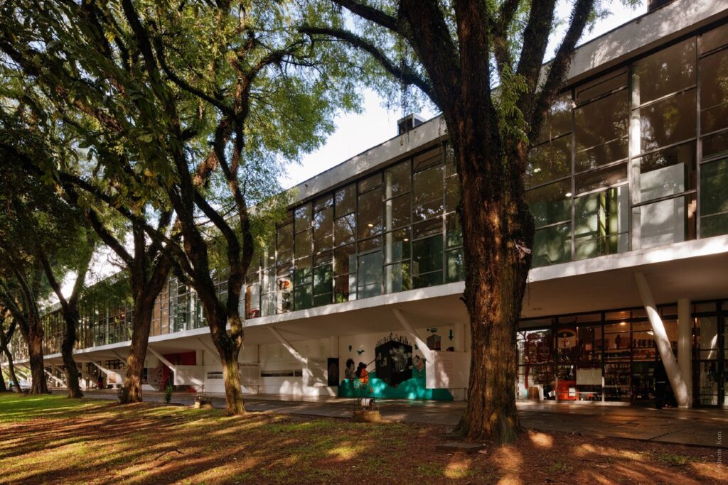 Fotografia da fachada do Museu fro Brasil, contornado por árvores e com parede envidraçada.