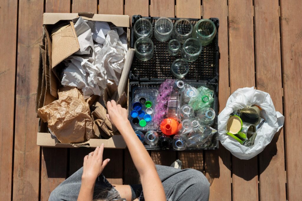 Pessoa separando o lixo de acordo com sua composição, entre papel, vidro, plástico e lata.