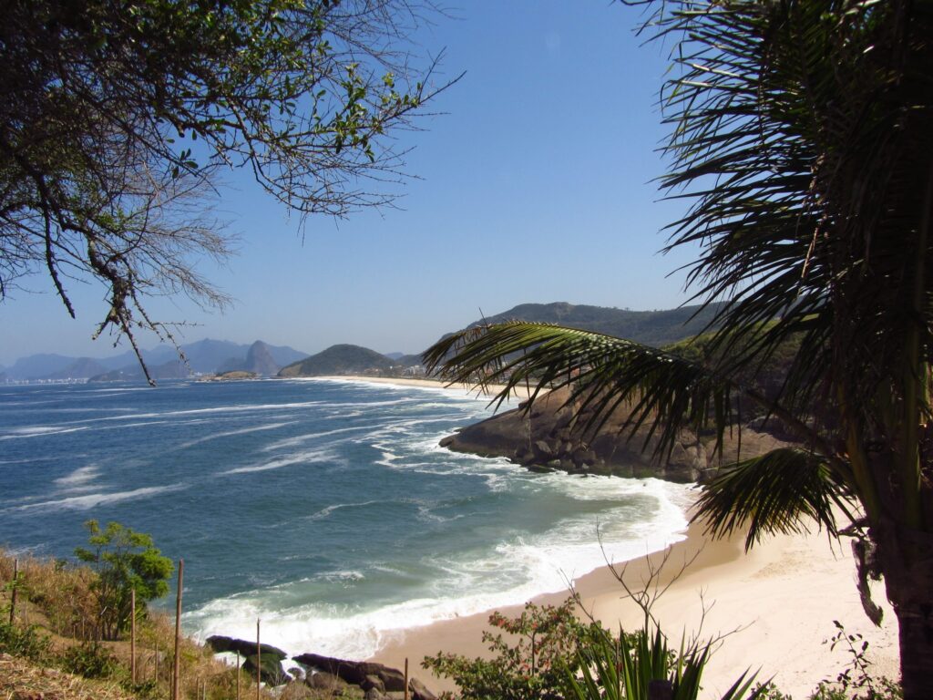 Praia do Sossego, com um mar agitado e vegetação em primeiro plano. 